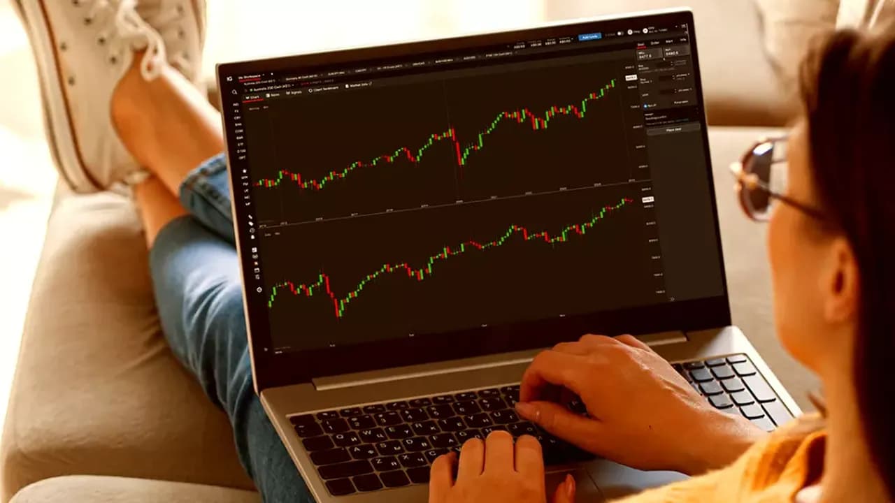 Person viewing stock market graphs on a laptop while sitting comfortably on a couch with legs crossed.